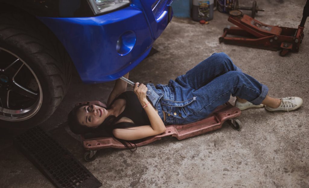 Woman working under a car with a creeper